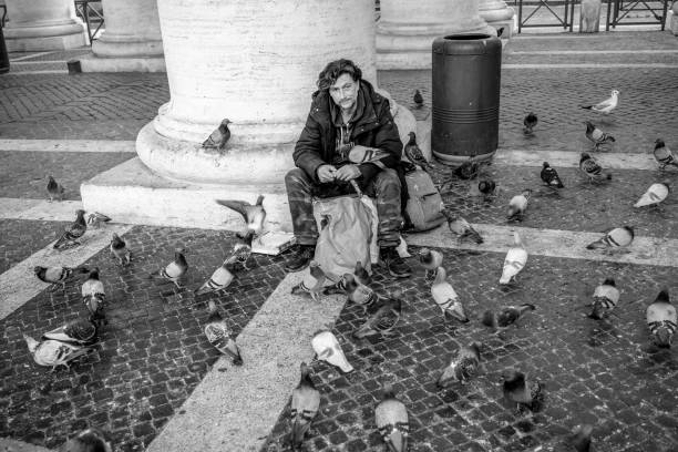 성 베드로 광장에 있는 베르니니의 식민지 아래에서 비둘기에게 음식을 제공하는 남자 - berninis colonnade 뉴스 사진 이미지
