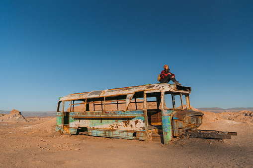Young Caucasian woman sitting on roof of abandoned bus in Atacama desert in Chile