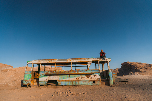 Young Caucasian woman sitting on roof of abandoned bus in Atacama desert in Chile