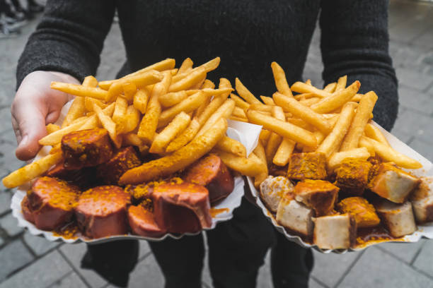 Woman hands holding traditional red and white curry wurst and french fries at Viktualienmarkt food market in Munich, Victuals Market Traditional german fast food. Red and white curry sausage with curry saude and fried potatoes take away at a food market in city center. weisswurst photos stock pictures, royalty-free photos & images