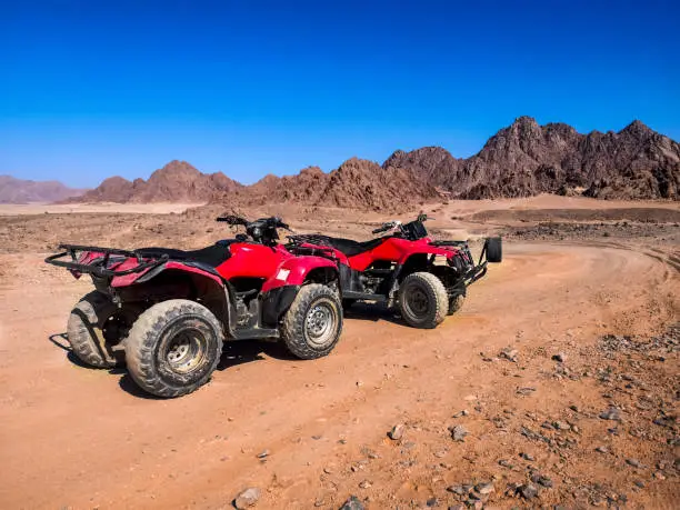 Two red quads stand near the mountains in the South Sinai desert near Sharm El Sheikh (Egypt). ATV safari concept, active leisure for tourists in desert, background with copy space