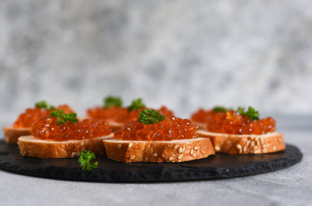 pan tostado con caviar rojo. sandwich con caviar y mantequilla sobre fondo de hormigón. - plank bread caviar close up fotografías e imágenes de stock