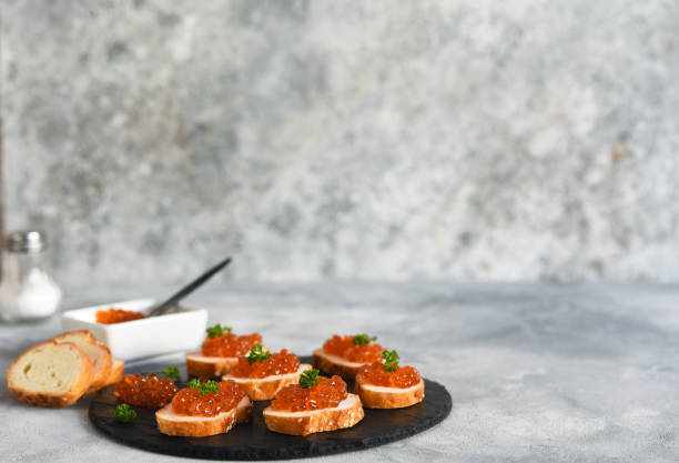 pão de torrada com caviar vermelho. sanduíche com caviar e manteiga em um fundo de concreto. - plank bread caviar close up - fotografias e filmes do acervo