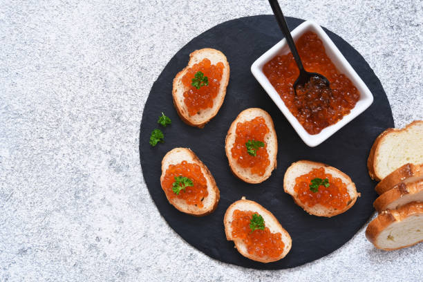 pão de torrada com caviar vermelho. sanduíche com caviar e manteiga em um fundo de concreto. - plank bread caviar close up - fotografias e filmes do acervo