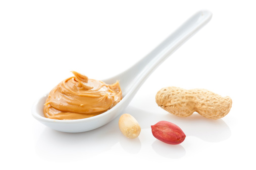 Creamy peanut butter in a white spoon with peanuts