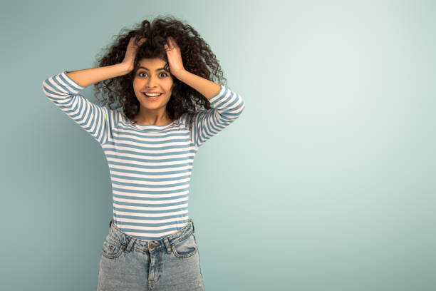 istock excited mixed race girl touching hair while looking at camera on grey background 1202242191