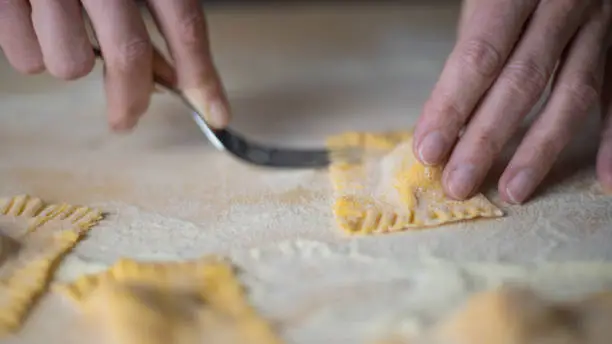 Photo of Closeup process making ravioli vegan homemade pasta. Housewife cook closes with a fork 'tortelli di zucca', traditional italian pasta, woman cooking food on kitchen