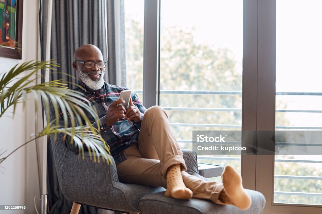 It's a wonderful thing to share in a connection Shot of a mature man using a cellphone while relaxing on a sofa at home Senior Adult Stock Photo