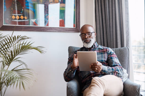 He enjoys some quality time with his smartest device Shot of a mature man using a digital tablet at home using digital tablet stock pictures, royalty-free photos & images