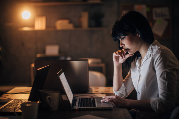 istock Young woman working late at night in office alone 1202259189