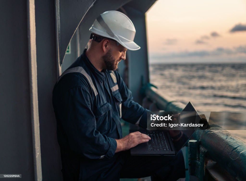 Marine chief officer or captain on deck of vessel or ship watching laptop Marine chief officer or captain on deck of vessel or ship watching laptop. Internet and home connection at sea. Sea Stock Photo
