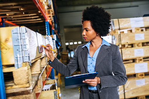 Mid adult african american supervisor standing and looking at warehouse filling up paperwork document