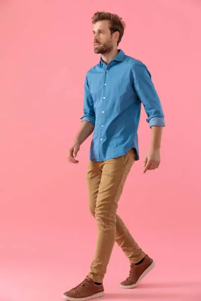 Photo of young casual man in denim shirt looking to side and walking