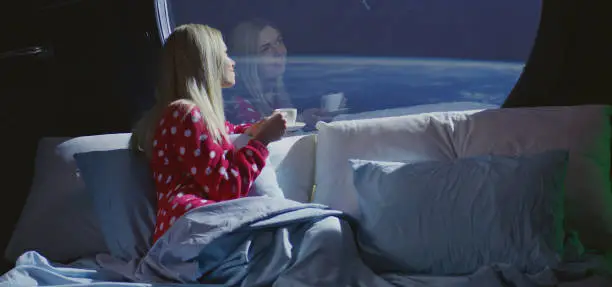 Medium shot of young woman enjoying the view and a cup of coffee in a spaceship