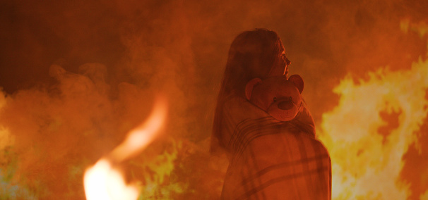 Medium shot of a girl trapped in fire crying for help while holding her teddy bear