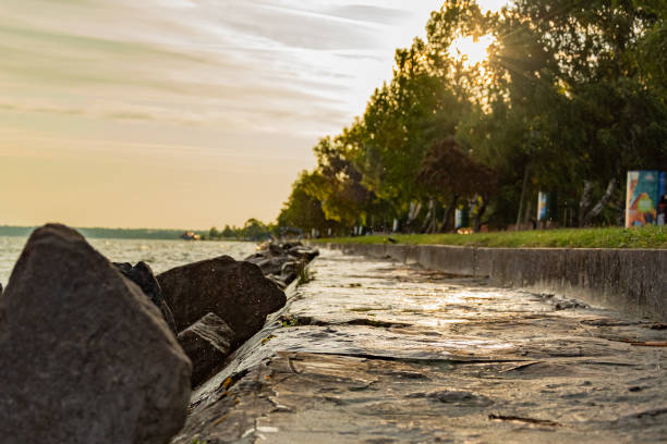 Rocky Balaton Lake coast at down. Picture shows the costline, the grass, the water and sky with the rising sun. Picture taken in Siofok town in summer 2019 - the most popular holiday destination in Hungary.