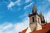 View of the sharp towers of the Church of Mother of God before Týn and red tiled roof against vibrant blue sky and white couds. Prague, Chezh Republic