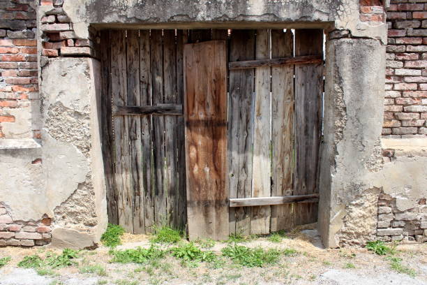 istock Backyard entrance doors made from dilapidated wooden boards mounted on red bricks wall of abandoned suburban family house 1202273179