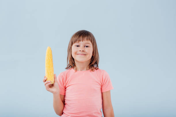 istock smiling girl has a corn in her hand. isolated on blue background, copy space, in studio, profile view 1202273796