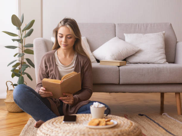 istock Cute girl reading book, sitting on floor at home, empty space 1202273824