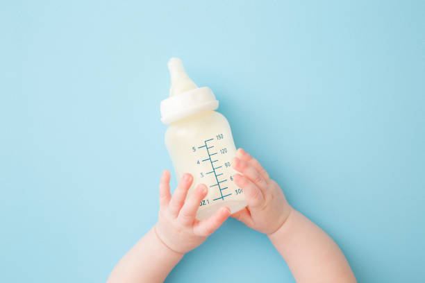 水色の床の背景に牛乳のボトルを保持する幼児の手。給餌時間。パステルカラー。クローズ アップ。視点ショット。上から下のビュー。 - 瓶 写真 ストックフォトと画像