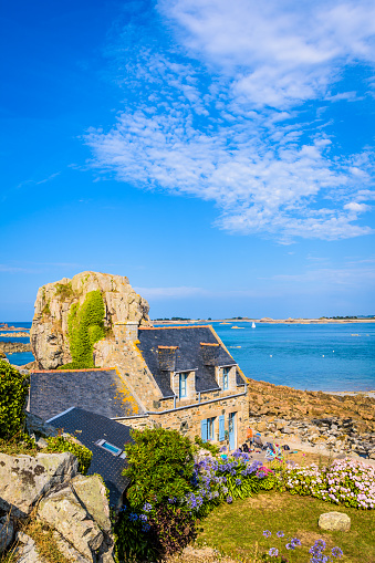 Plougrescant, France - August 3, 2019: Typical breton granite house with slate roof in the small harbor of Pors Hir in northern Brittany, built on the seashore next to a boulder, by a sunny summer day