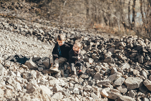 Children sitting on the stones on shore of lake. Concept of family vacation.