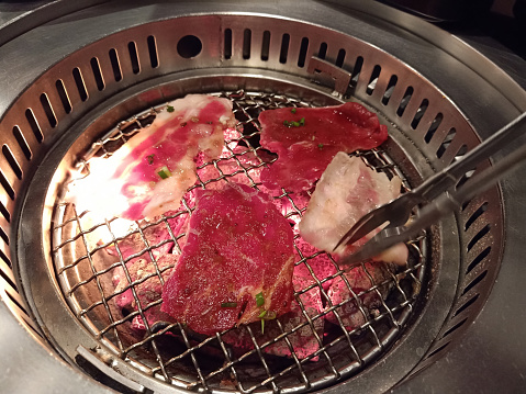 Roast beef Sizzling Korean BBQ on mesh grill of charcoal fire ( Bulgogi ).Table set of korean barbecue, meat , pork, Kimchi, rice, vegetables, sauce and hood, ready for grilling in Korean restaurant