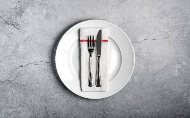 istock White plate with eating utensils (cutlery) and a folded napkin on a rustic cracked concrete background 1202282188