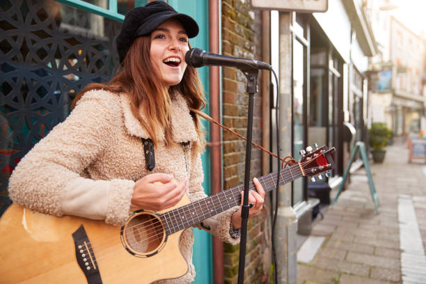 weibliche musiker in busking spielen akustische gitarre und singen im freien in street - street musician stock-fotos und bilder
