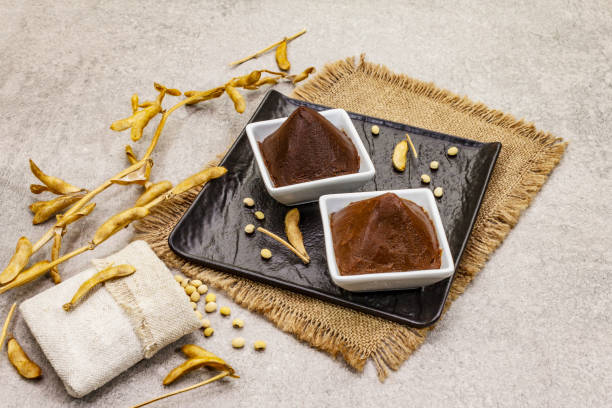 istock Miso paste, traditional Japanese seasoning. Two types, dark and light brown with dry soya beans. Sackcloth, bag, pods. Stone concrete background 1202285206