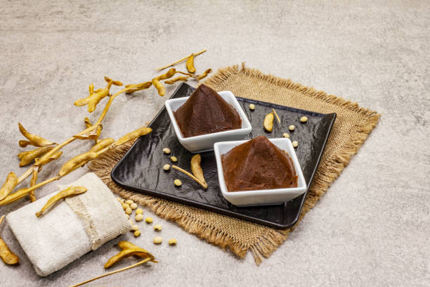 istock Miso paste, traditional Japanese seasoning. Two types, dark and light brown with dry soya beans. Sackcloth, bag, pods. Stone concrete background 1202285211
