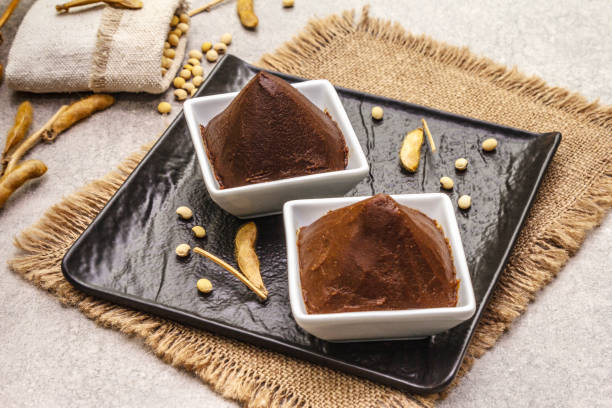 istock Miso paste, traditional Japanese seasoning. Two types, dark and light brown with dry soya beans. Sackcloth, bag, pods. Stone concrete background 1202285300