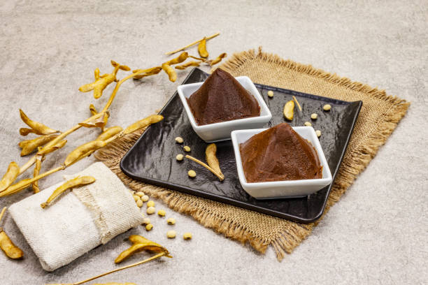 istock Miso paste, traditional Japanese seasoning. Two types, dark and light brown with dry soya beans. Sackcloth, bag, pods. Stone concrete background 1202285575