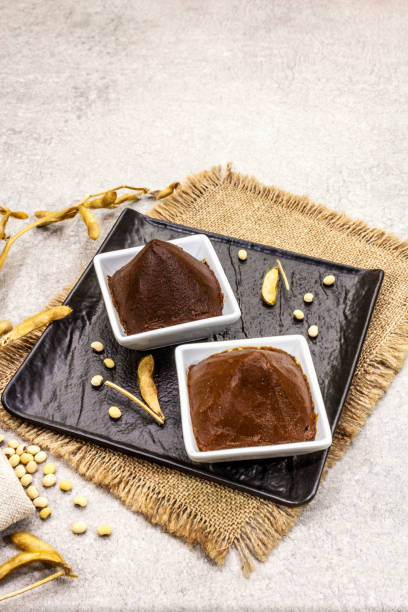 istock Miso paste, traditional Japanese seasoning. Two types, dark and light brown with dry soya beans. Sackcloth, bag, pods. Stone concrete background 1202285621