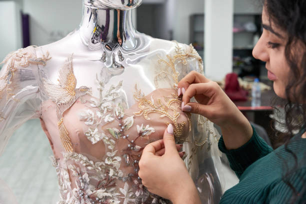 istock Dressmaker fixing white lace wedding dress on a mannequin in tailor studio 1202285678