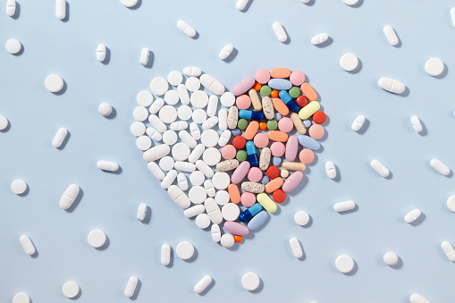 White pills with colored pills were arranged as heart shape on blue background