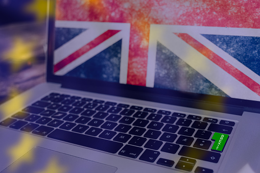 Green enter button for brexit on a computer keyboard. The Union Jack on the computerscreen, and the blurred EU stars as overlay