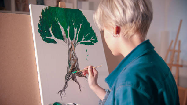 istock A young blonde woman draws a tree with paints in the studio 1202296589