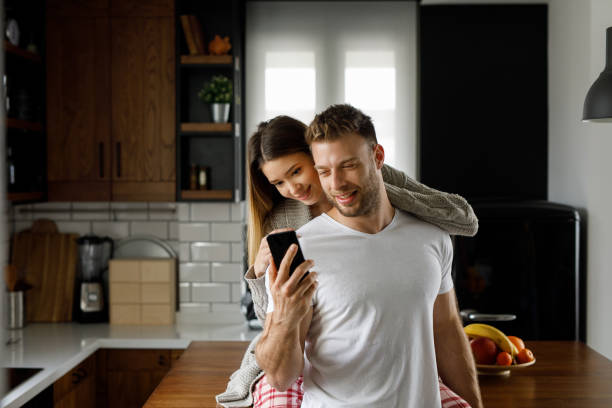 istock Young affectionate couple looking at mobile phone in the kitchen 1202298375