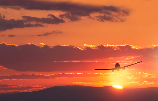 The silhouette of the plane flies against the backdrop of a beautiful bright sunset and mountains. Beautiful landscape.