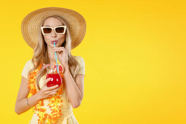 istock Attractive lady with hat on head hold beverage in hands isolated on yellow background 1202301942