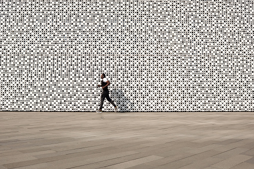 Workout in urban background. Black sportsman in activewear running along contemporary building with white perforated facade, copy space