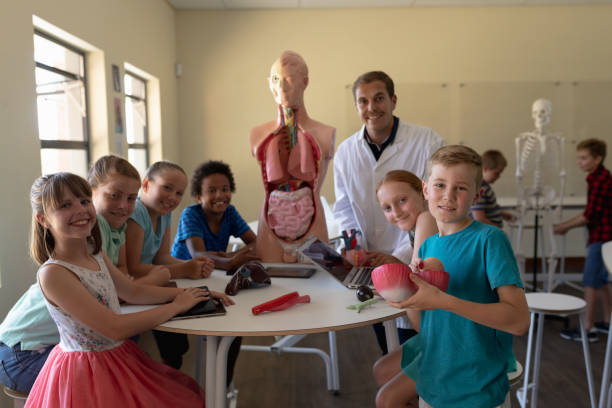 istock Male teacher wearing a lab coat and school pupils using anatomy model 1202306364