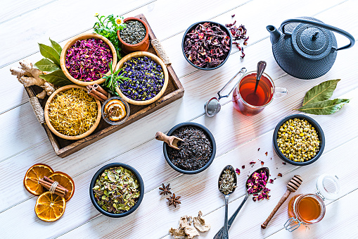 Herbal tea. Large variety of dried herbs and flowers for preparing healthy detox infusions shot from above on white table. The composition includes dried part of plants like hibiscus, calendula, rose petals, chamomile, green tea, bay leaves, cinnamon sticks, ginger, lemons, mint leaves, a honey jar and dried orange slices among others. A tea cup and a black teapot are also included. High resolution 42Mp studio digital capture taken with Sony A7rii and Zeiss Batis 40mm F2.0 CF lens