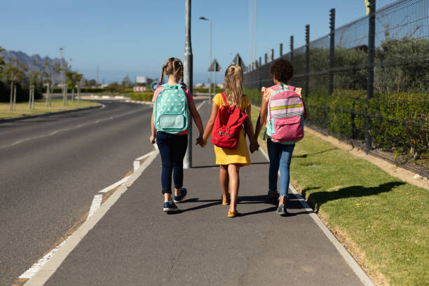 istock Three schoolgirls walking along a road to elementary school 1202308635