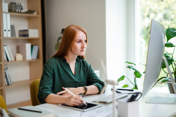 オフィスの屋内デスクに座っている若いビジネスウーマンは、コンピュータを使って。 - long hair red hair women men ストックフォトと画像