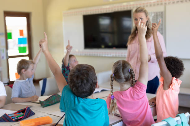 istock Group of schoolchildren raising their hands in an elementary school classroom 1202312085