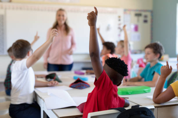 istock Group of schoolchildren raising their hands in an elementary school classroom 1202312090