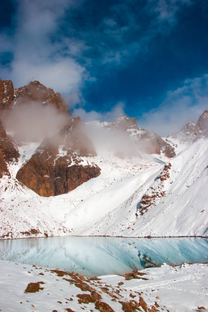 istock The mountain lake is surrounded by snow peaks. Mountains behind clouds. 1202312300